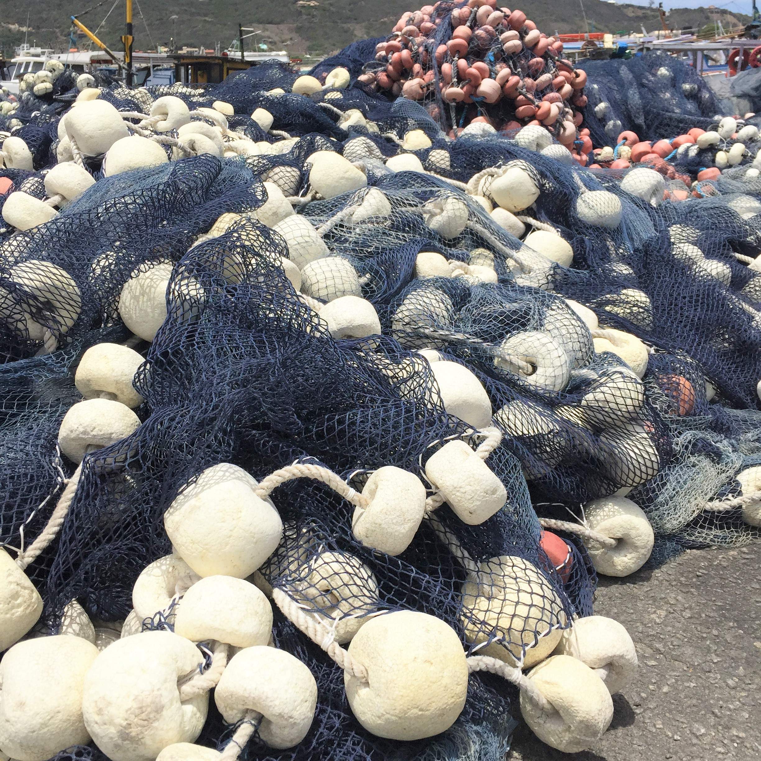 Rede de pesca repousada no chão com barco ao fundo